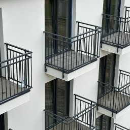 DATO Install - Elewacja budynku z balkonami z czarnymi, metalowymi balustradami, widok z dołu pod kątem.