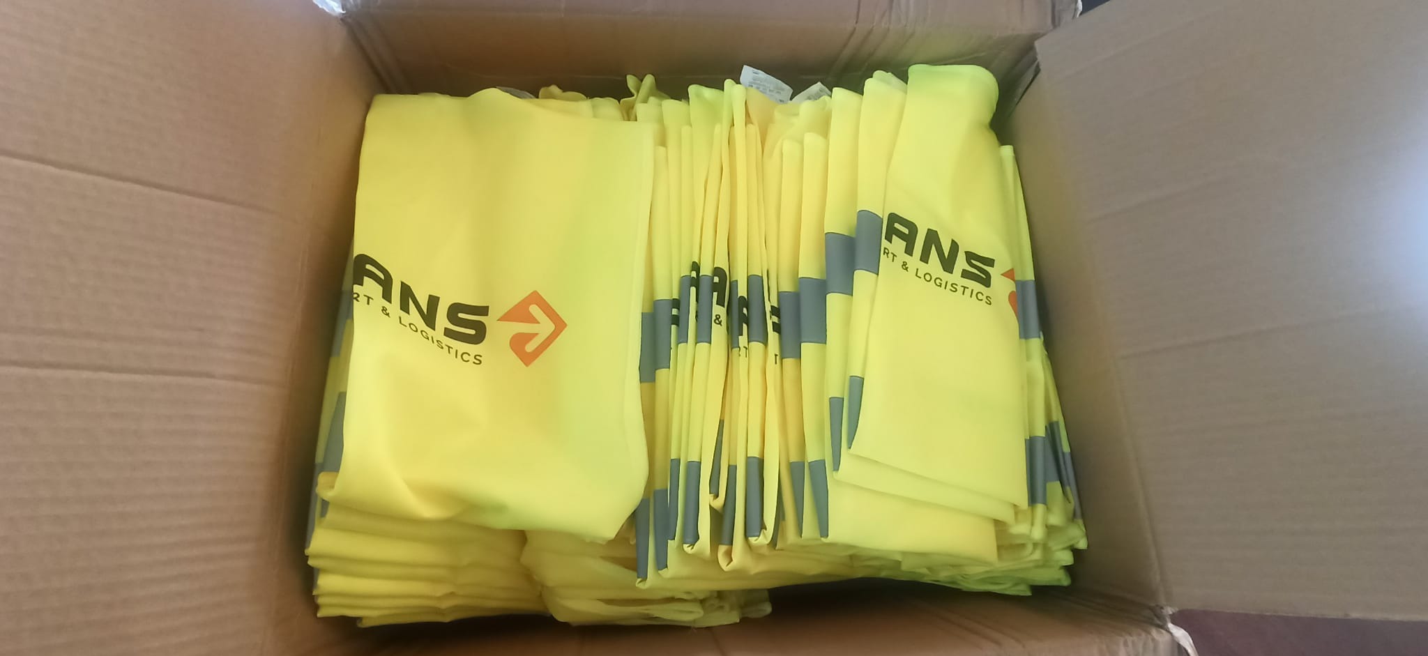 Żółte torby z nadrukiem logo ANS Transport & Logistics w kartonowym pudle. Torby ułożone równo, widoczne detale nadruku i materiału.