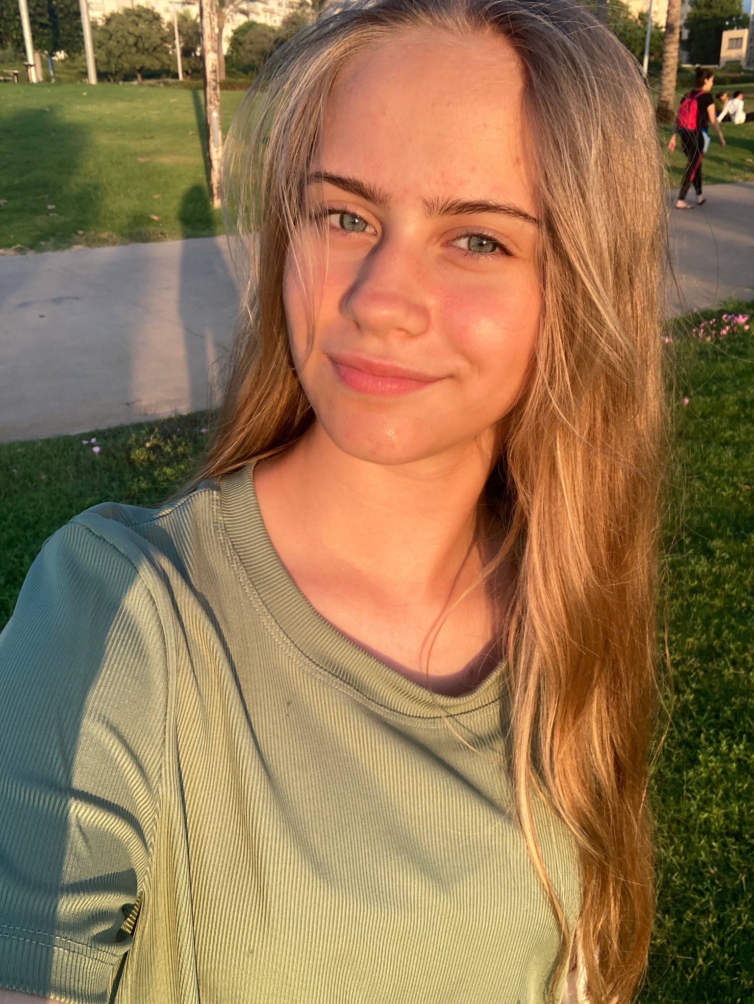 Portret uśmiechniętej młodej kobiety z długimi blond włosami na tle parku w promieniach zachodzącego słońca.