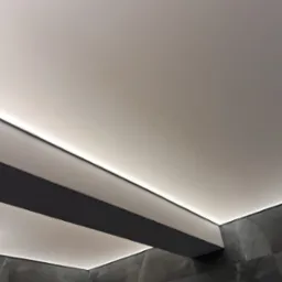 Nowoczesny sufit z podwieszaną konstrukcją i oświetleniem LED, ciemna marmurowa ściana w tle. Minimalistyczny design wnętrza.