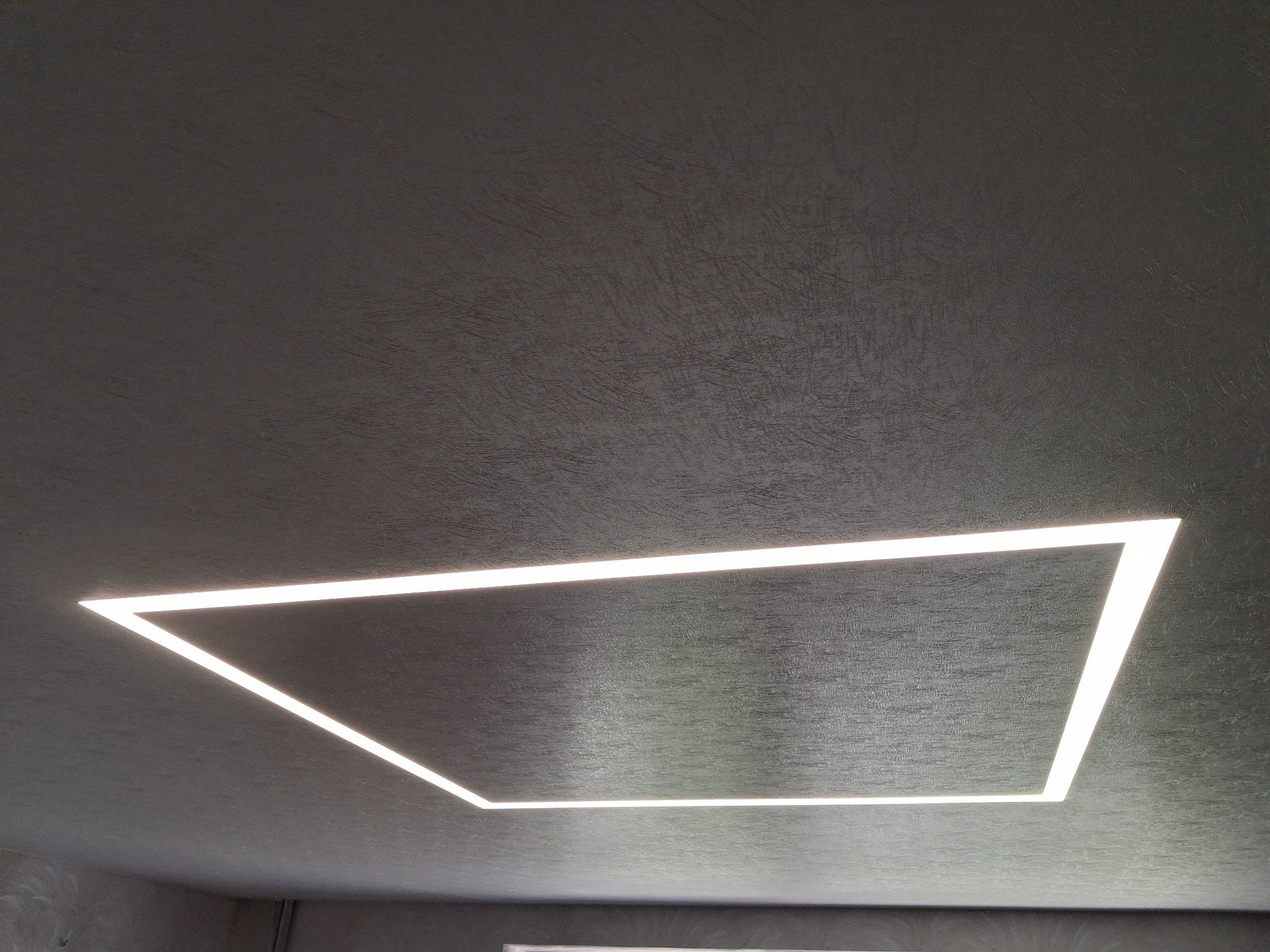 Szary sufit z fakturą, oświetlony prostokątną, wpuszczoną lampą LED, tworzącą nowoczesny design wnętrza. Minimalistyczne oświetlenie.