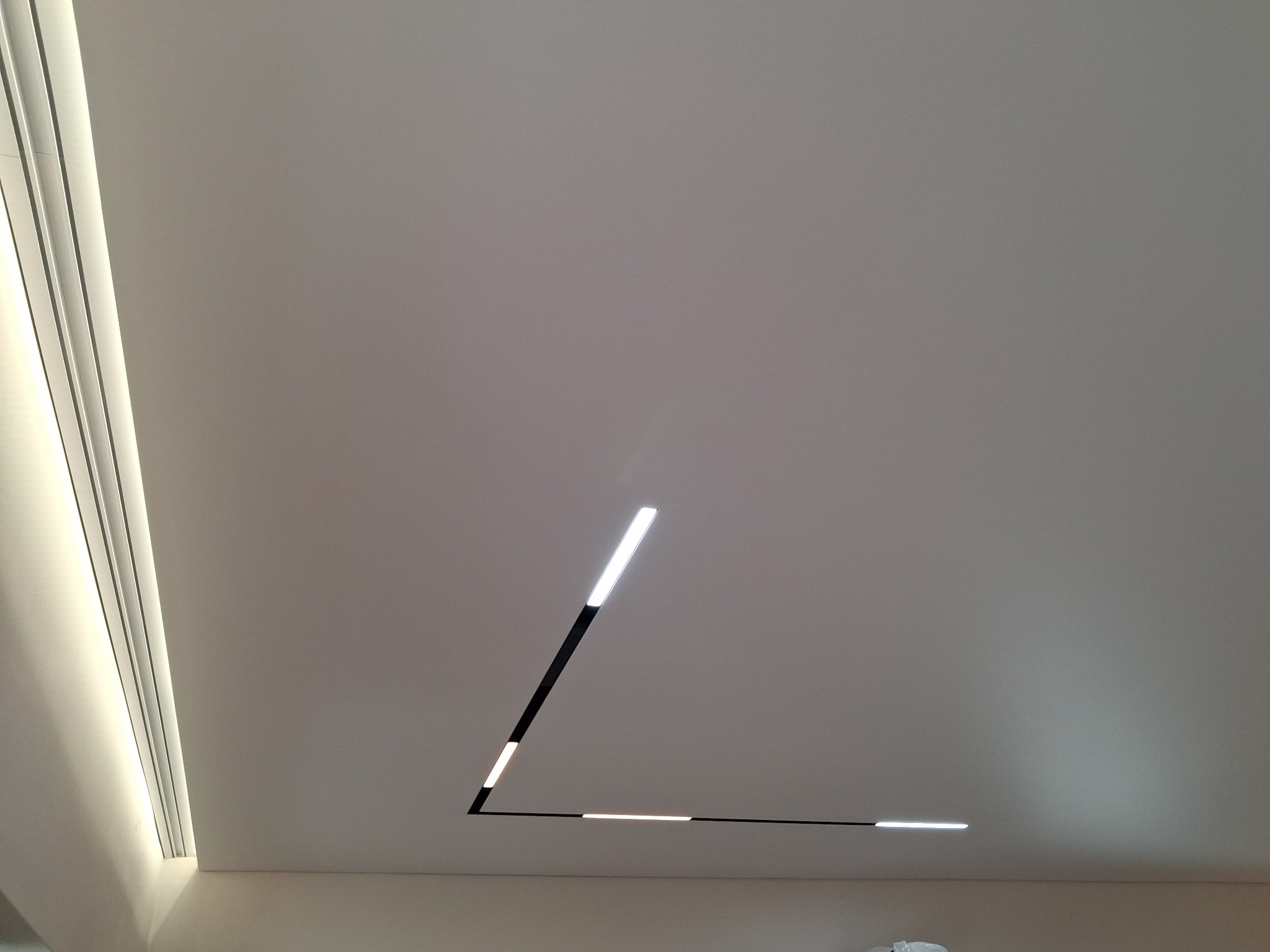 Nowoczesny, minimalistyczny sufit z liniowym oświetleniem LED w kształcie litery L, Bielsko-Biała. Biała powierzchnia, subtelne światło, designerski detal.