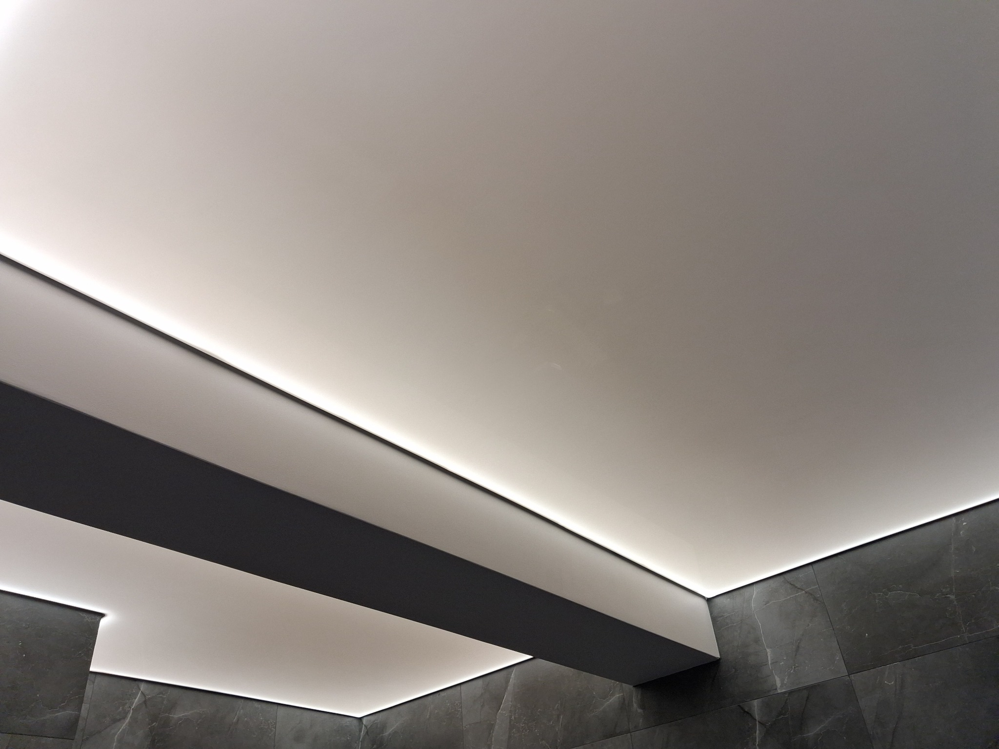 Nowoczesny sufit z podwieszaną konstrukcją i oświetleniem LED, ciemna marmurowa ściana w tle. Minimalistyczny design wnętrza.