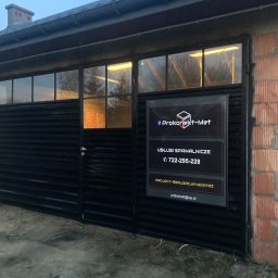 Prokonekt-met - Czarna brama wjazdowa z poziomych profili zamontowana w budynku z cegły dziurawki, z tabliczką reklamową firmy Prokonekt-Met oferującej usługi spawalnicze.