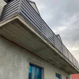 Prokonekt-met - Metalowa balustrada balkonowa z poziomych profili, zamontowana na surowym betonowym balkonie budynku w trakcie budowy, okna zabezpieczone folią.