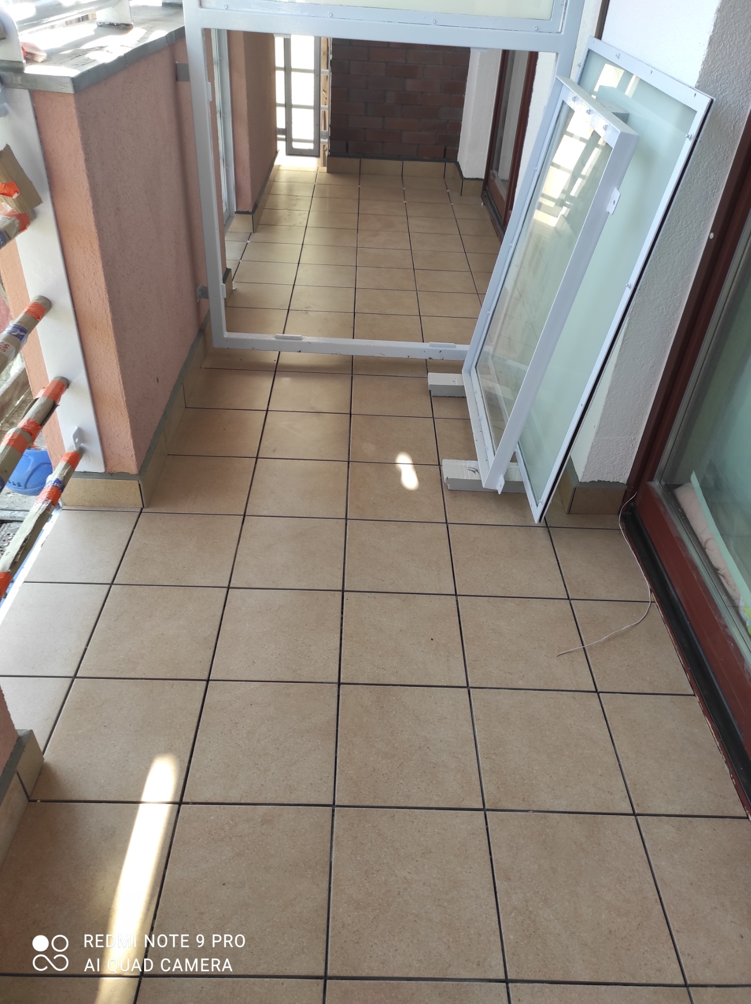 Balkon z beżową terakotą i przygotowanymi do montażu białymi ramami okiennymi, widoczne narzędzia i materiały zabezpieczone folią.