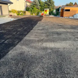 Przygotowanie podłoża pod trawnik z rolki: wyrównana powierzchnia z piaskiem kwarcowym, widoczne worki z piaskiem, plac zabaw w tle.