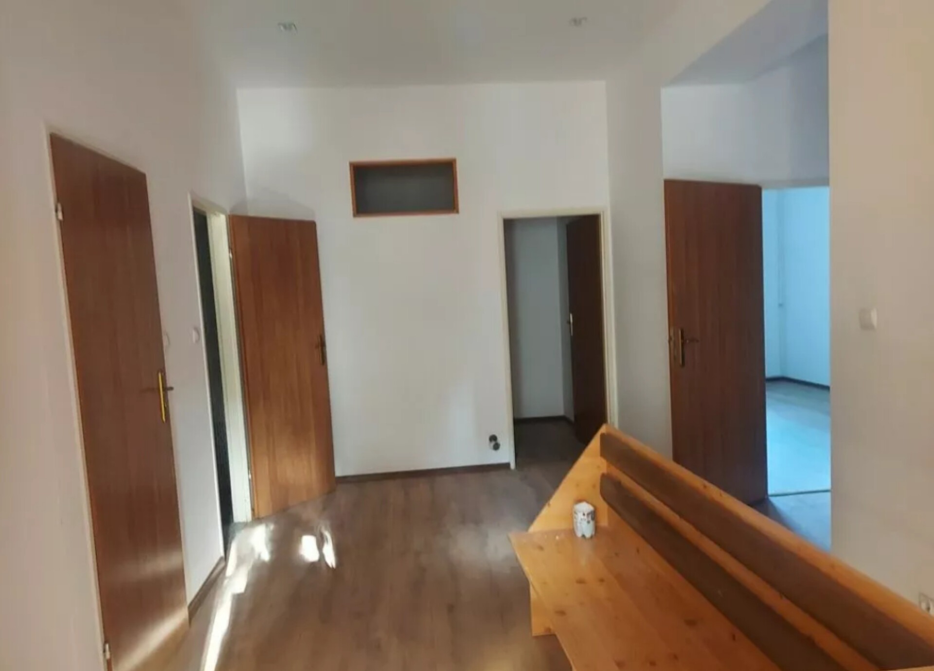 Jasne wnętrze po remoncie: świeżo pomalowane białe ściany, drewniana podłoga, kilka otwartych drzwi z drewnianymi ościeżnicami, widoczny fragment drewnianej ławki.