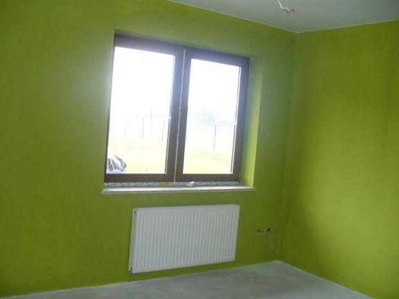 Świeżo pomalowany pokój w Oleśnicy na kolor zielony, widoczne okno z brązową ramą i biały grzejnik pod nim.
