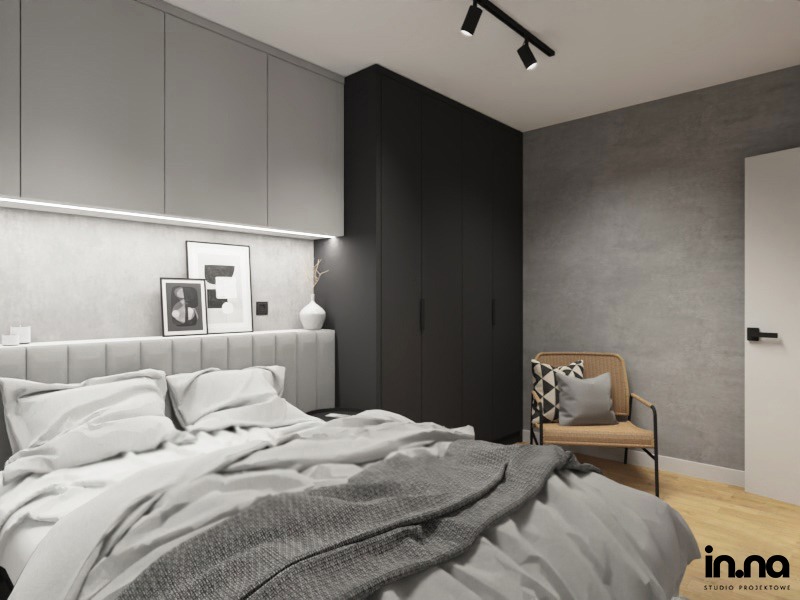 Nowoczesna sypialnia w odcieniach szarości i czerni, z dużym łóżkiem, szarą tapetowaną ścianą za wezgłowiem, czarną szafą i rattanowym fotelem z poduszką.