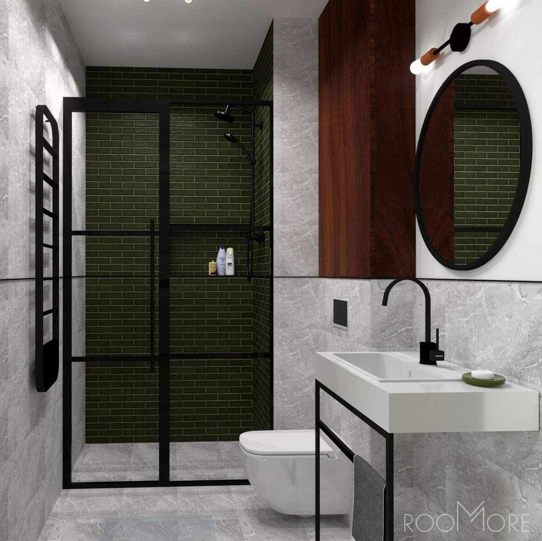 Nowoczesna łazienka z zielonymi płytkami typu cegiełka w kabinie prysznicowej, białą umywalką na czarnym stelażu, okrągłym lustrem i drewnianym panelem dekoracyjnym.