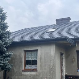 Lilek Usługi Dekarskie - Dom z nowym, grafitowym dachem z dachówki, z oknem dachowym i kominem z cegły, widoczny fragment elewacji w trakcie prac wykończeniowych i srebrny świerk.