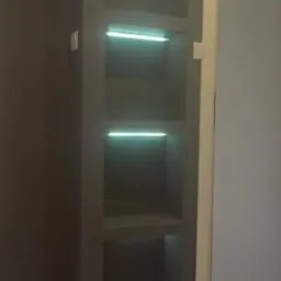 Wnęka ścienna z półkami, podświetlona listwami LED, szara ściana i białe listwy przypodłogowe, widok z dołu.