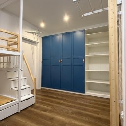 Kompleksowe wykończenie wnętrz Serhii Bakharev - Pokój dziecięcy po remoncie: drewniana podłoga, zabudowa z szafami w kolorze granatowym, białe regały i łóżko piętrowe z drabinką.