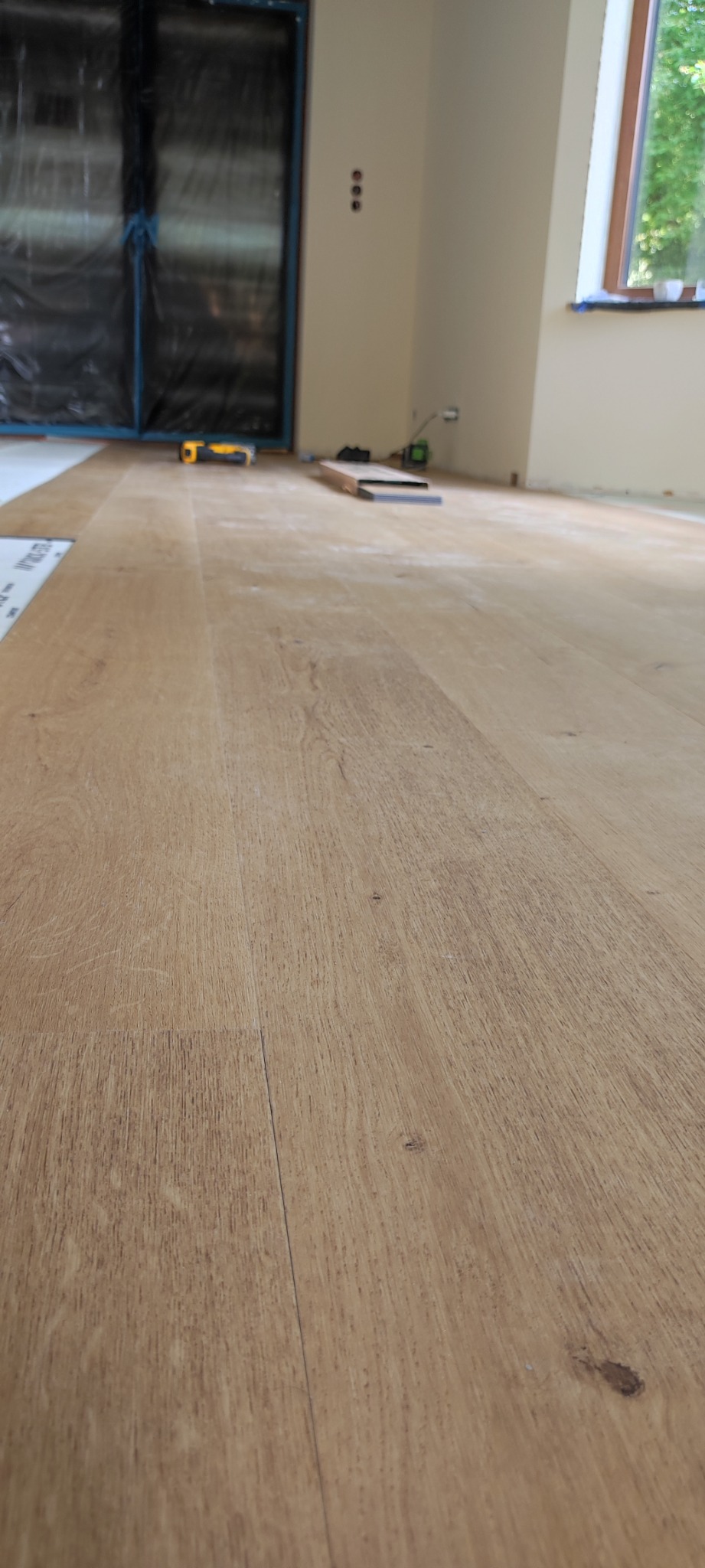 Ułożony parkiet w jasnym odcieniu drewna, z widocznymi narzędziami i folią zabezpieczającą w tle, sugerujący trwający proces wykończenia wnętrza.