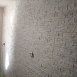 Wnętrze z wykończoną ścianą imitującą kamień, widoczna drabina malarska i gniazdko elektryczne.