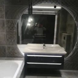 Nowoczesna łazienka w Jeleniej Górze z umywalką nablatową na podświetlanej szafce, widoczna wanna i lustro z odbijającym się fotografem.