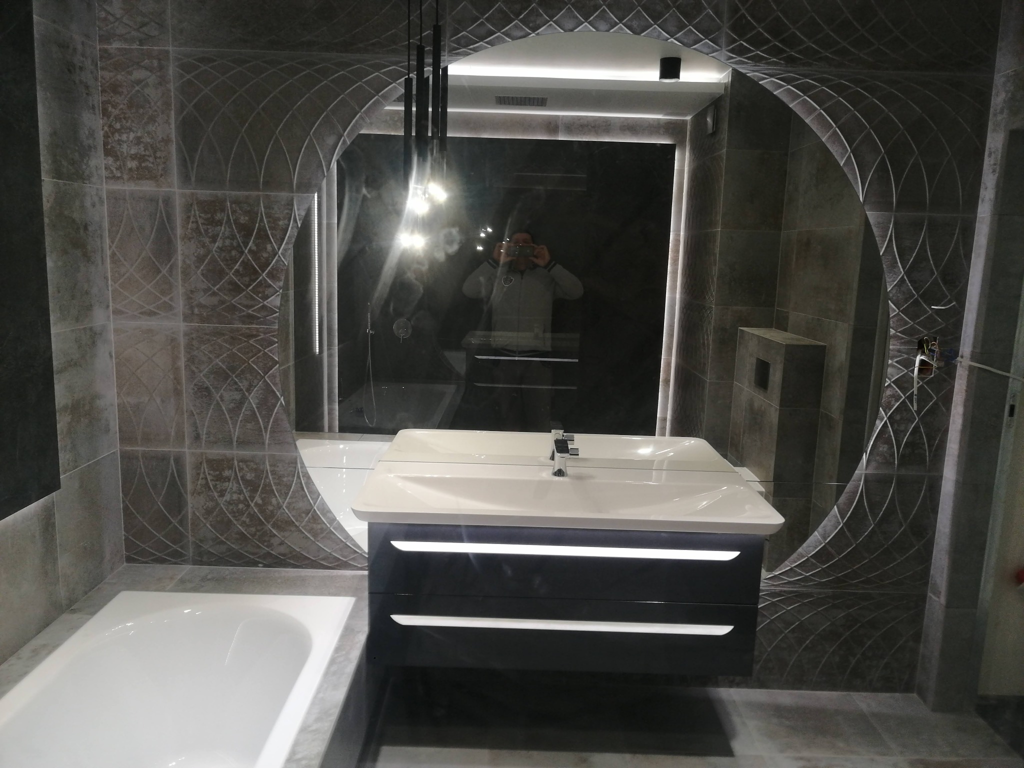 Nowoczesna łazienka w Jeleniej Górze z umywalką nablatową na podświetlanej szafce, widoczna wanna i lustro z odbijającym się fotografem.