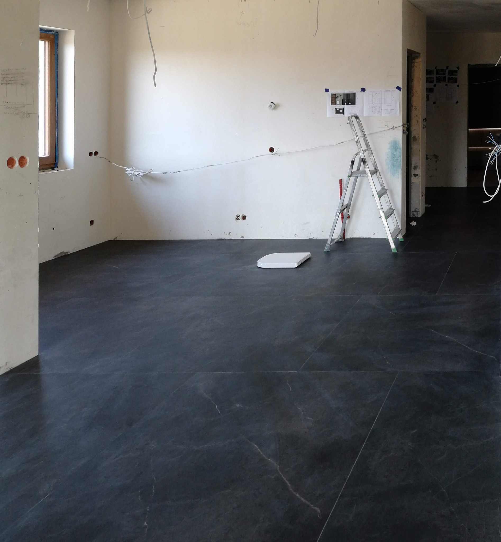 Ciemna, marmurkowa posadzka w trakcie remontu, z widocznymi przewodami elektrycznymi i drabiną w tle.