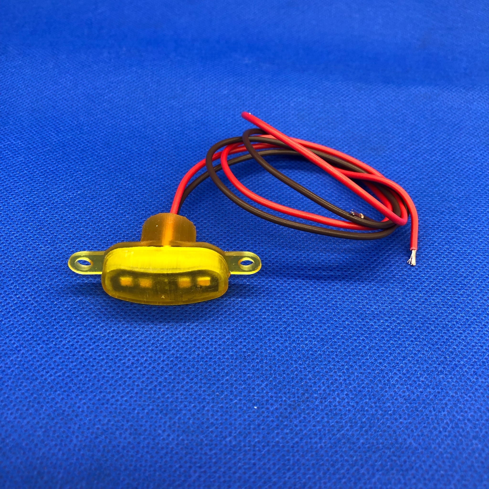 Żółta dioda LED z przewodami czerwonym i czarnym leżąca na niebieskim tle.