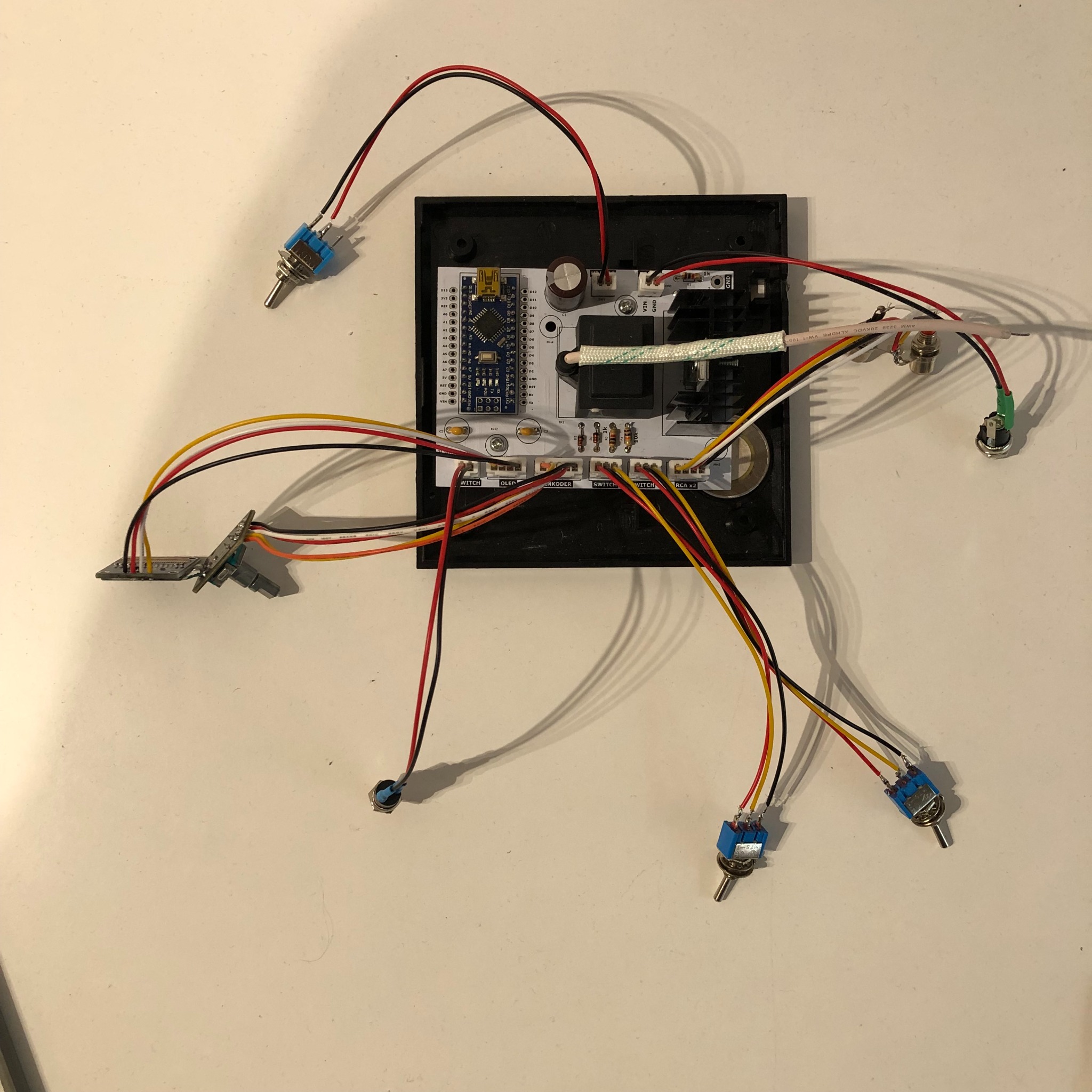 Elektroniczna płytka prototypowa z mikrokontrolerem, przełącznikami, gniazdami i przewodami, zamontowana w czarnej obudowie, widok z góry na białym tle.