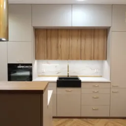 Nowoczesna kuchnia w odcieniach beżu i drewna z czarnym zlewem farmerskim i złotą armaturą, parkiet w jodełkę na podłodze.