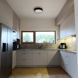 Rafał Rytwiński - Jasna kuchnia z szarymi, matowymi frontami szafek, drewnianym blatem i podłogą ułożoną w jodełkę, z widocznym logo firmy na pierwszym planie.