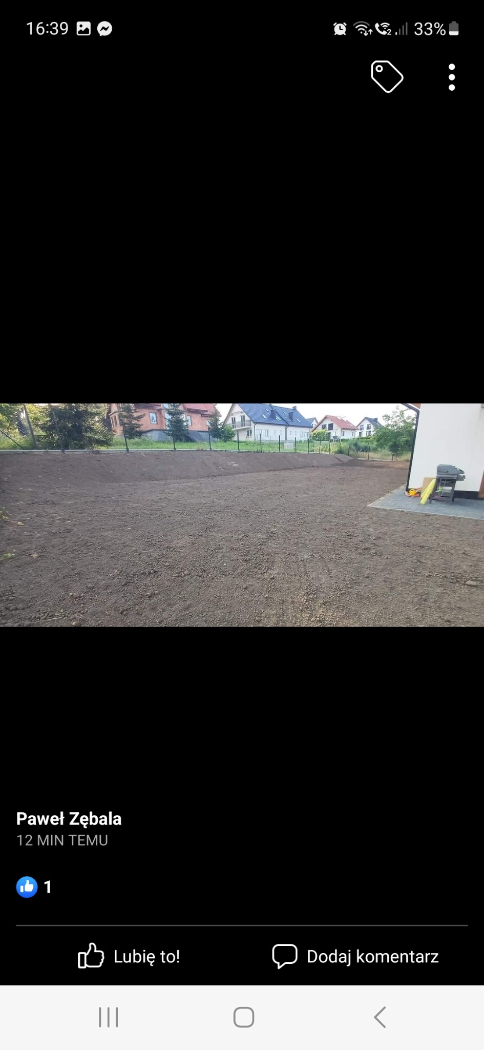 Wyrównany teren działki budowlanej z widocznymi domami w tle, przygotowany pod dalsze prace.