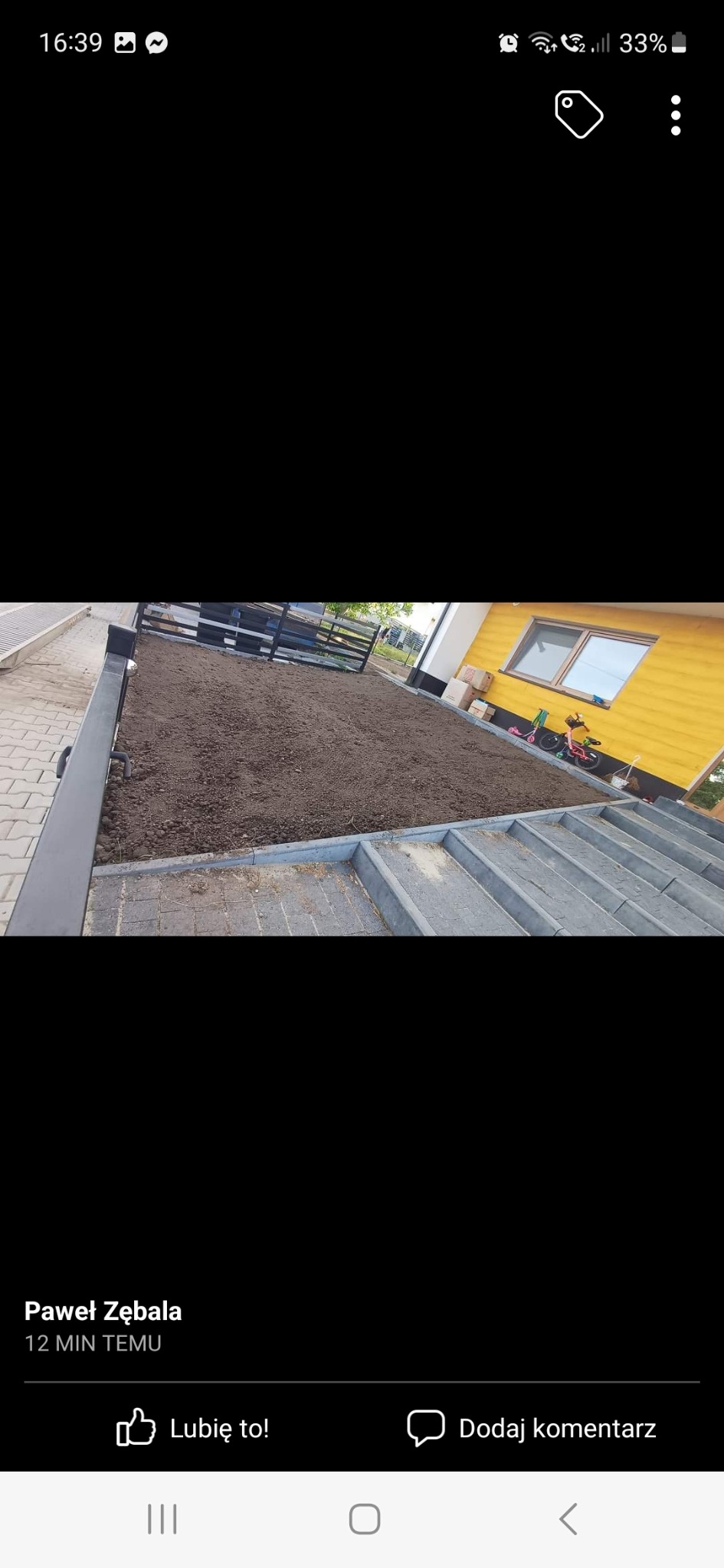 Przygotowany teren pod trawnik lub nasadzenia, obrzeża z kostki, widoczny fragment żółtej elewacji budynku i ogrodzenie.