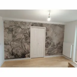 Pokój po remoncie z tapetą w kwiaty i białą dwuskrzydłową szafą wnękową, widoczny fragment podłogi z jasnego parkietu i grzejnik.