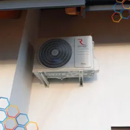 Zewnętrzna jednostka klimatyzatora Rotenso Revio Series zamontowana na białej ścianie budynku, zabezpieczona kolcami przeciw ptakom.