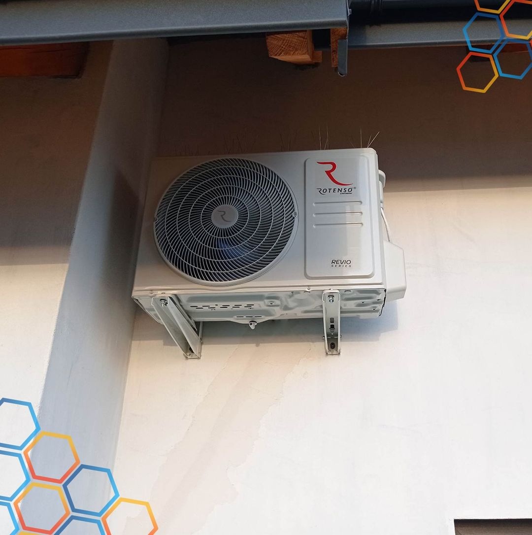 Zewnętrzna jednostka klimatyzatora Rotenso Revio Series zamontowana na białej ścianie budynku, zabezpieczona kolcami przeciw ptakom.