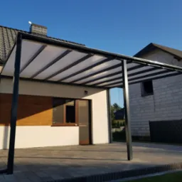 Nowoczesna, wolnostojąca wiata garażowa z czarną, metalową konstrukcją i przezroczystym zadaszeniem poliwęglanowym, przylegająca do domu z drewnianą elewacją.