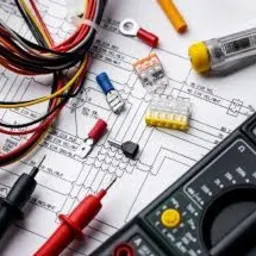 Multimetr, przewody elektryczne, złączki WAGO i schemat instalacji elektrycznej na białym tle. Widoczne końcówki kablowe i próbnik napięcia.