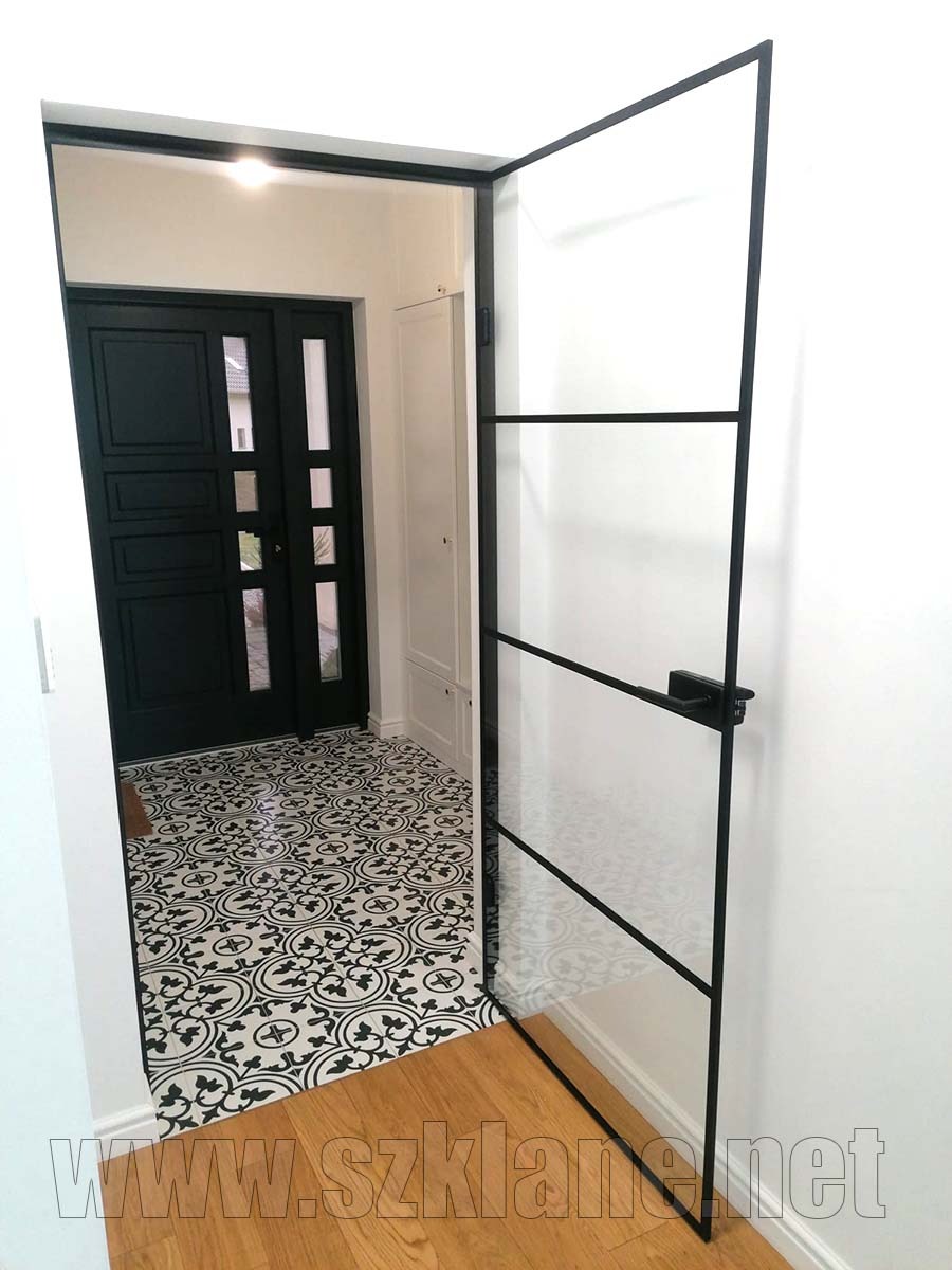 Szklane drzwi wewnętrzne z czarną ramą, otwarte, widoczne z wnętrza domu, z wzorzystą podłogą i drewnianym parkietem, w tle czarne, klasyczne drzwi.