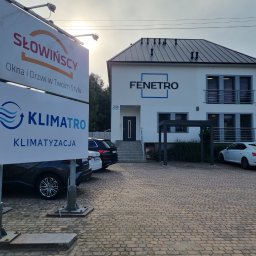 FENETRO SPÓŁKA Z OGRANICZONĄ ODPOWIEDZIALNOŚCIĄ SPÓŁKA KOMANDYTOWA - Budynek firmy z szyldem reklamowym oferującym okna, drzwi i systemy chłodzenia, zaparkowane samochody na brukowanym podjeździe.