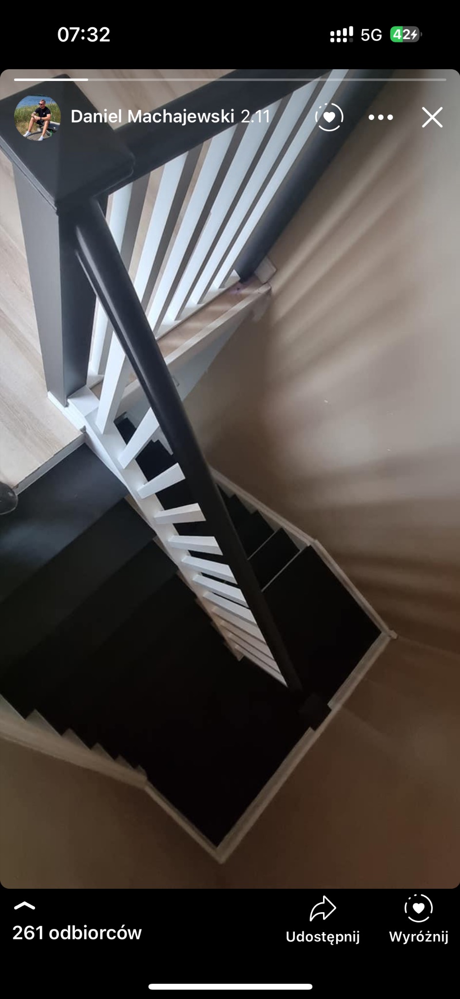 Widok z góry na spiralne schody z czarnymi stopniami i białymi barierkami w jasnym wnętrzu.