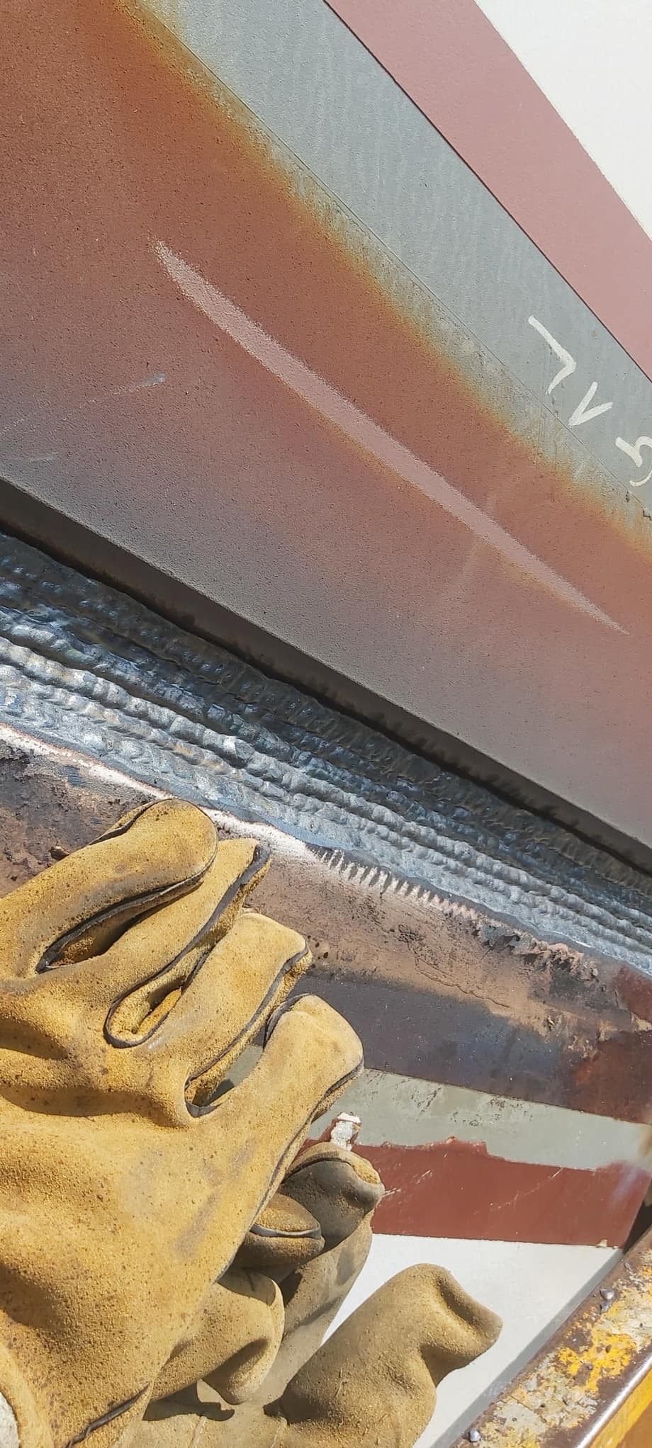 Zbliżenie na spoiny na metalowej konstrukcji, widoczne w rękawicy ochronnej, z lekkim zabrudzeniem i śladami użytkowania.