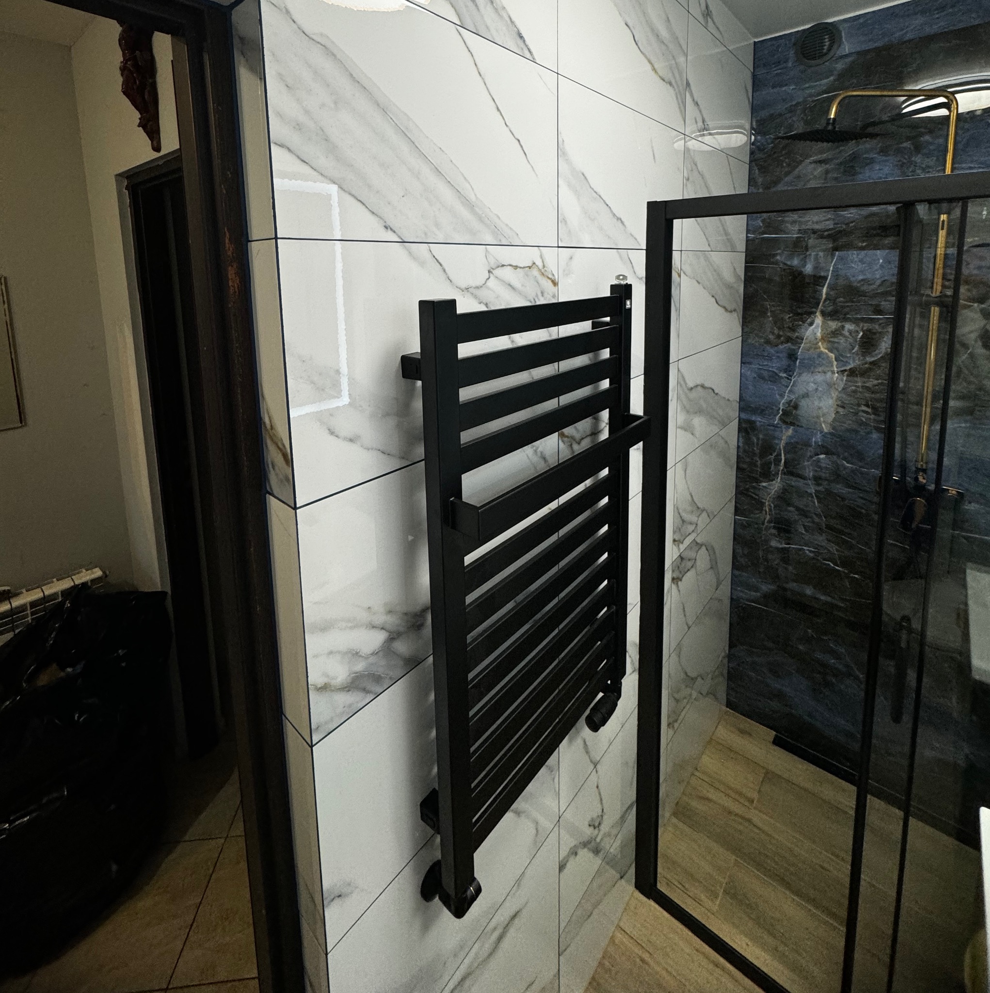 Czarny grzejnik łazienkowy na ścianie z marmurowymi płytkami w nowoczesnej łazience z kabiną prysznicową.