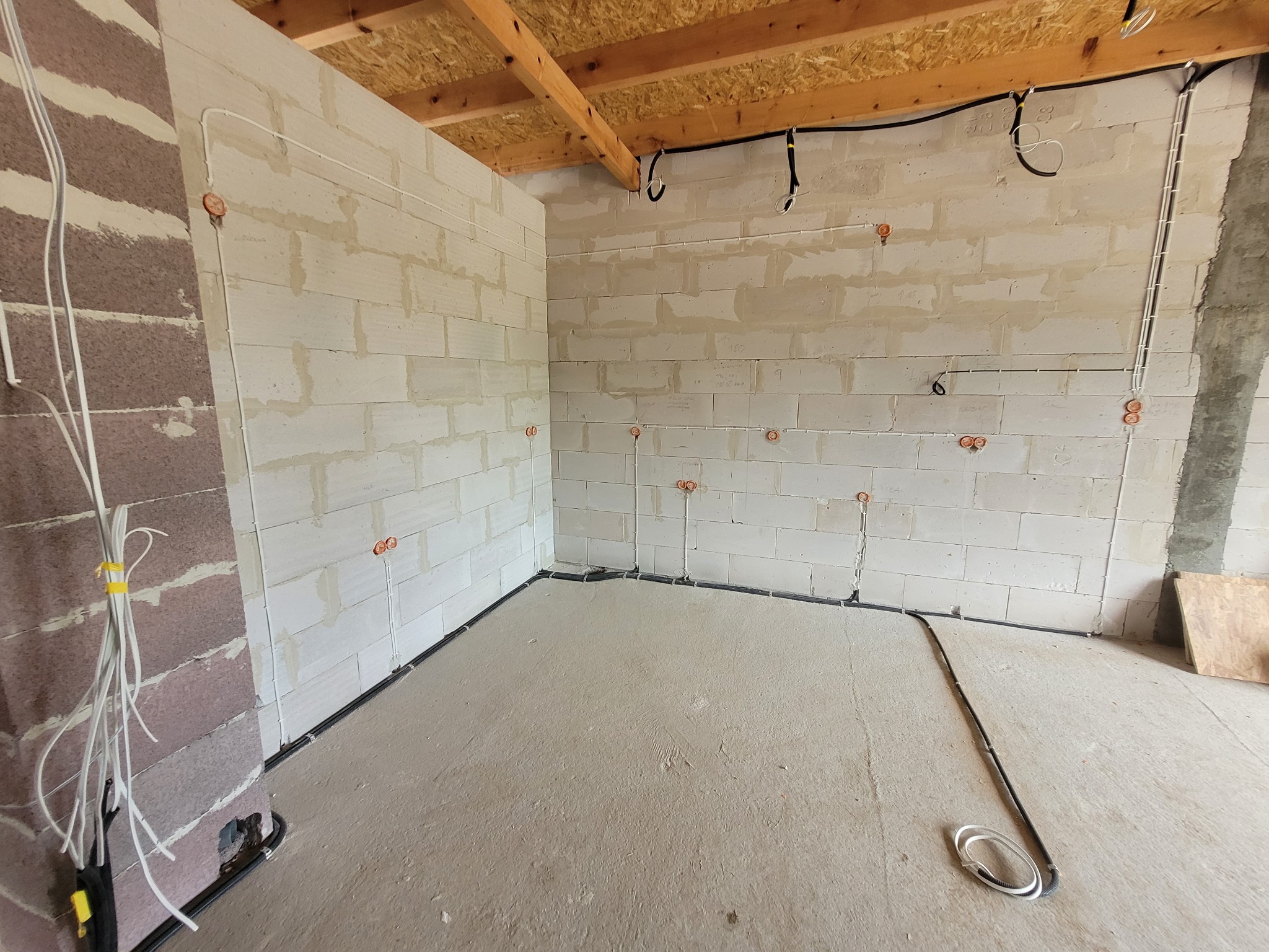 Surowy stan: Instalacja elektryczna w nowo budowanym pomieszczeniu z widocznymi przewodami w peszlach i puszkami instalacyjnymi na ścianach z betonu komórkowego oraz niezabezpieczonymi przewodami...