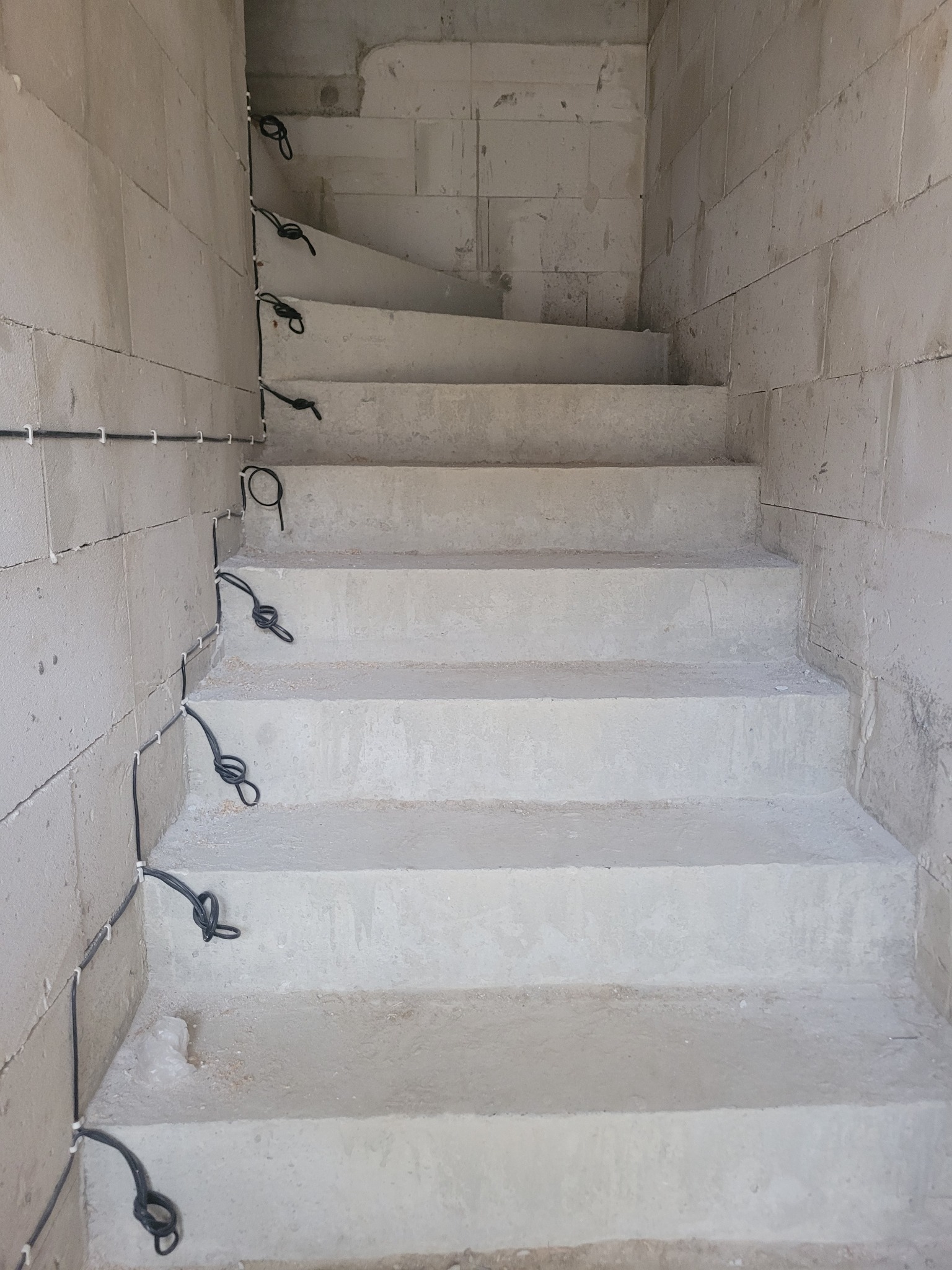 Surowe betonowe schody w trakcie budowy z widocznymi kablami elektrycznymi przymocowanymi do ściany za pomocą uchwytów.