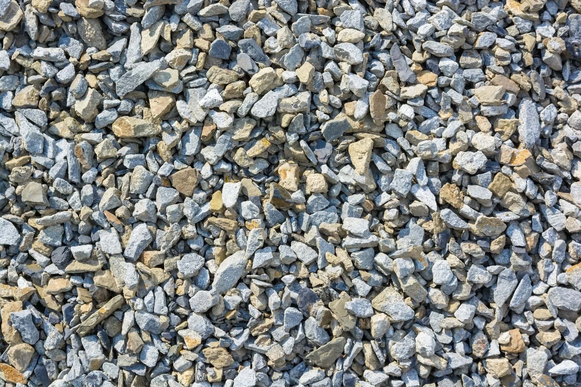Drobny, jasnoszary i beżowy kamień kruszony różnej wielkości, wypełniający całą powierzchnię kadru, oświetlony jasnym światłem słonecznym.