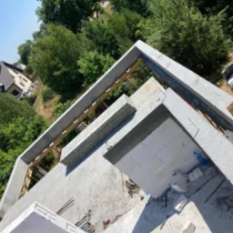 Wznoszenie ścian z bloczków betonu komórkowego Ytong Silka z widocznym zbrojonym wieńcem na budowie domu jednorodzinnego w słoneczny dzień.