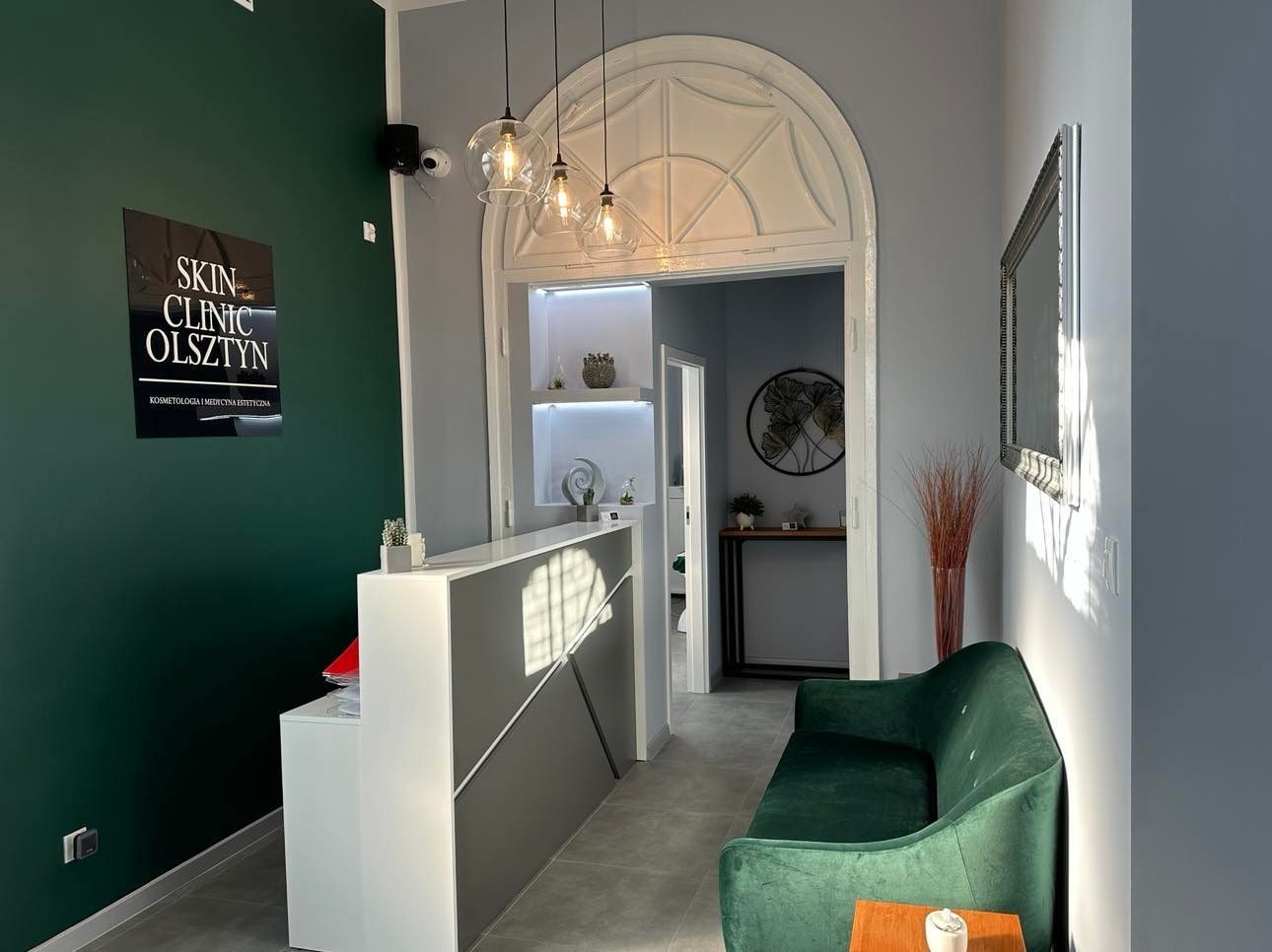 Recepcja kliniki z zieloną ścianą, logo Skin Clinic Olsztyn, nowoczesne oświetlenie i zielona sofa w poczekalni.