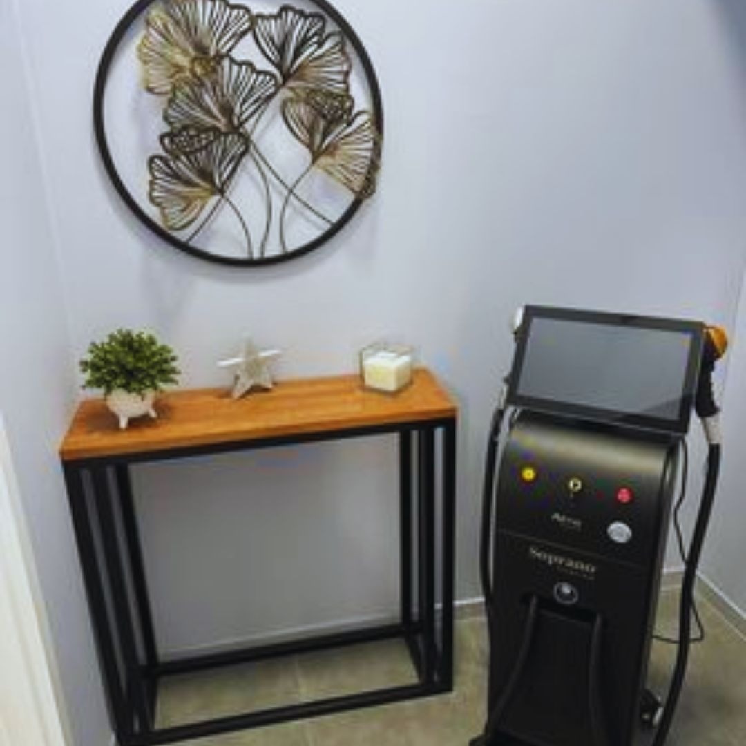 Wnętrze gabinetu z urządzeniem Soprano Ice Platinum do zabiegów, drewniany stolik z dekoracjami oraz okrągła ozdoba ścienna z motywem liści.