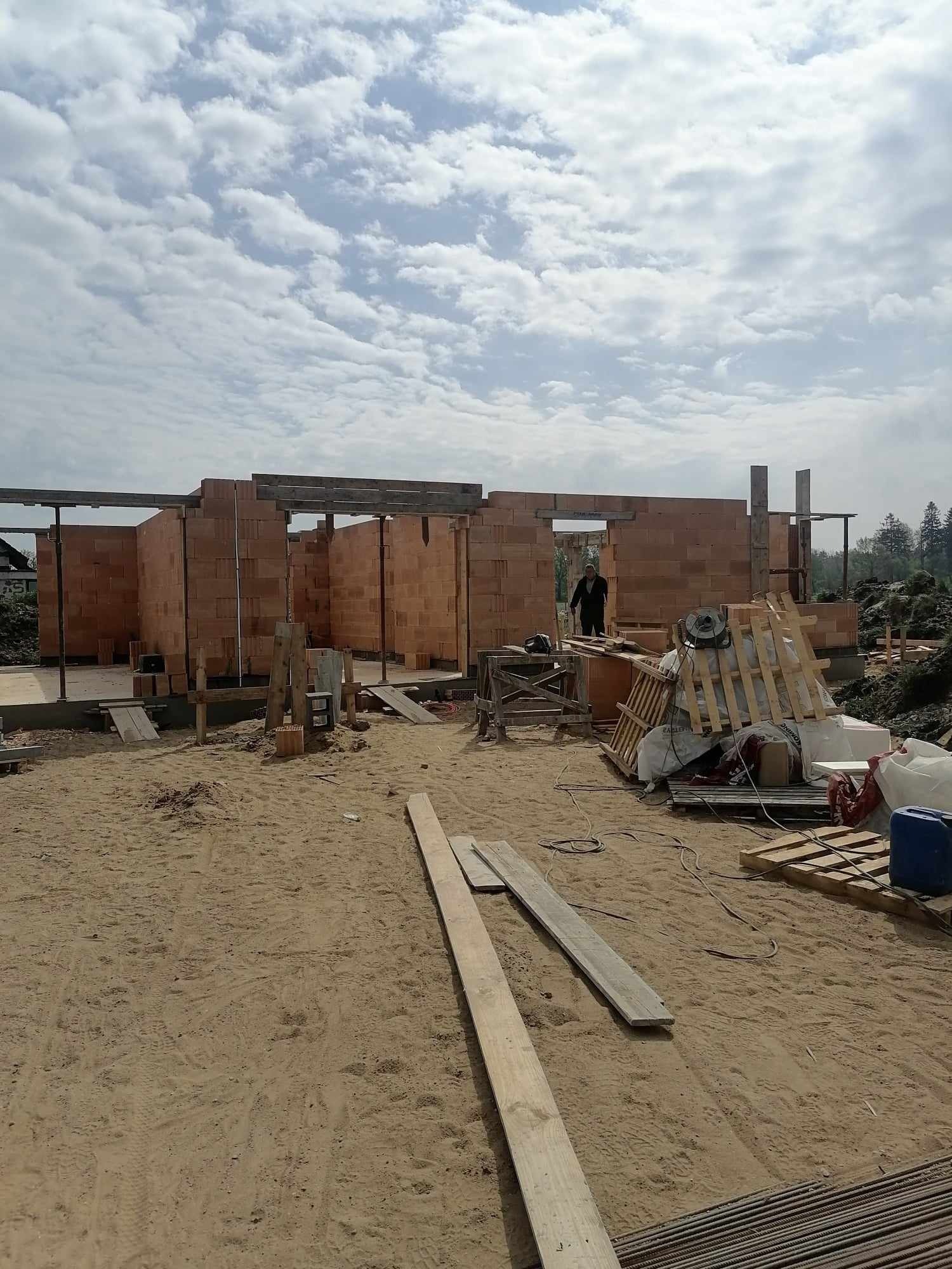 Wznoszenie ścian z cegły ceramicznej na budowie domu jednorodzinnego, widoczne rusztowania i materiały budowlane, pracownik w tle.