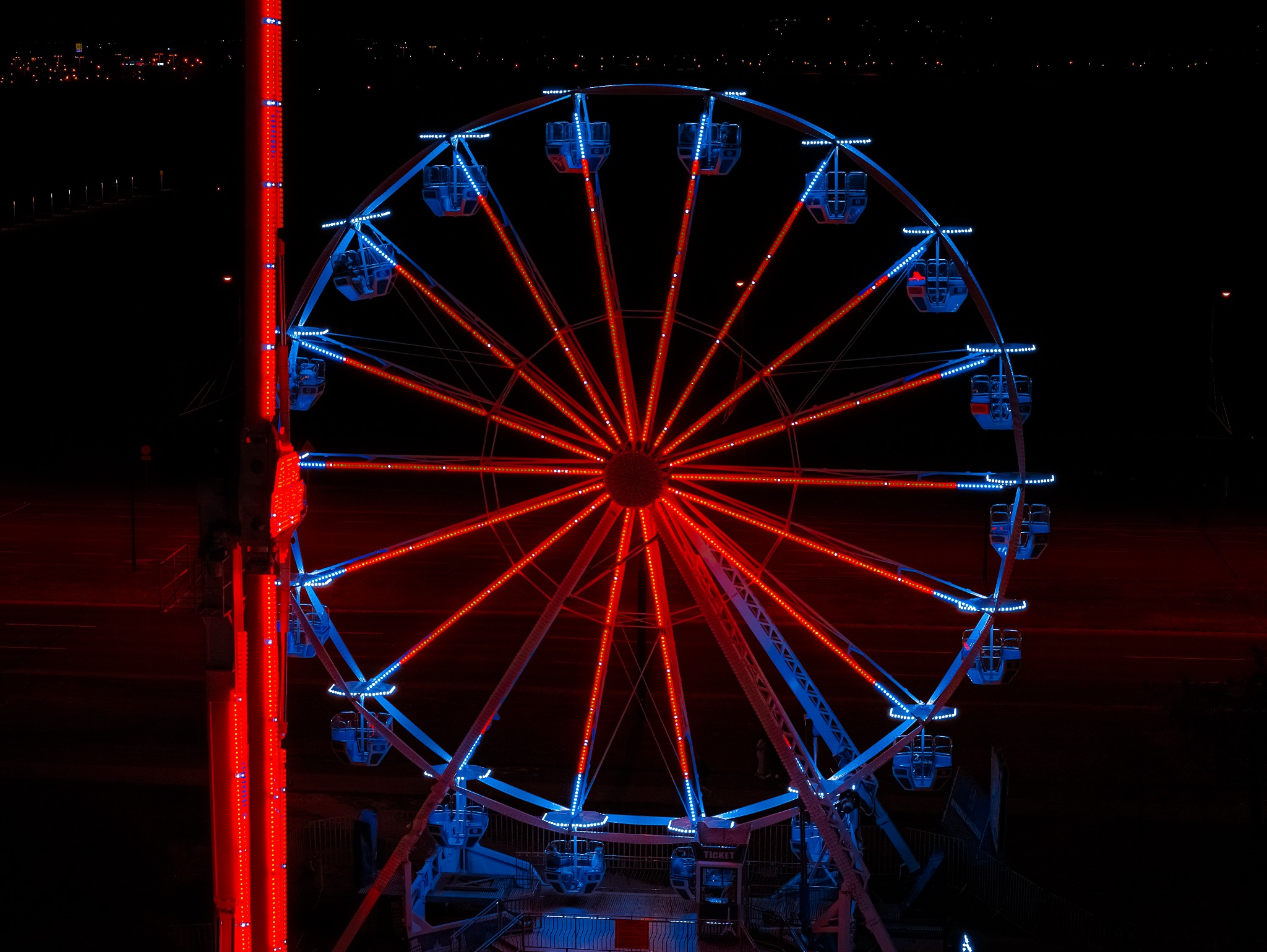 Oświetlone diabelskie koło w nocy, czerwone i niebieskie światła, ciemne tło.