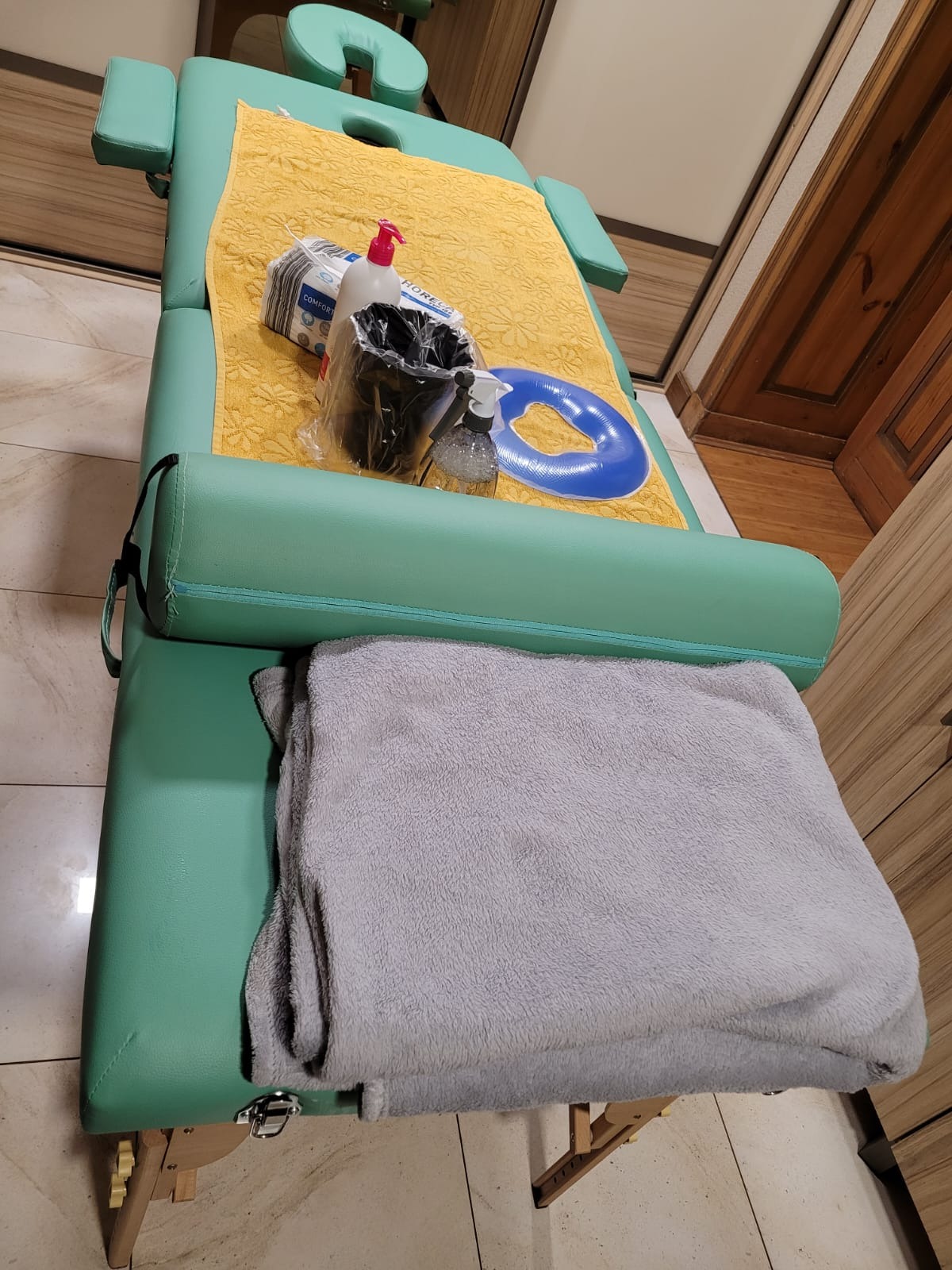 Zielony stół do zabiegów z żółtym ręcznikiem, niebieskim kołem, pojemnikiem na akcesoria i butelką z rozpylaczem, przygotowany do sesji.