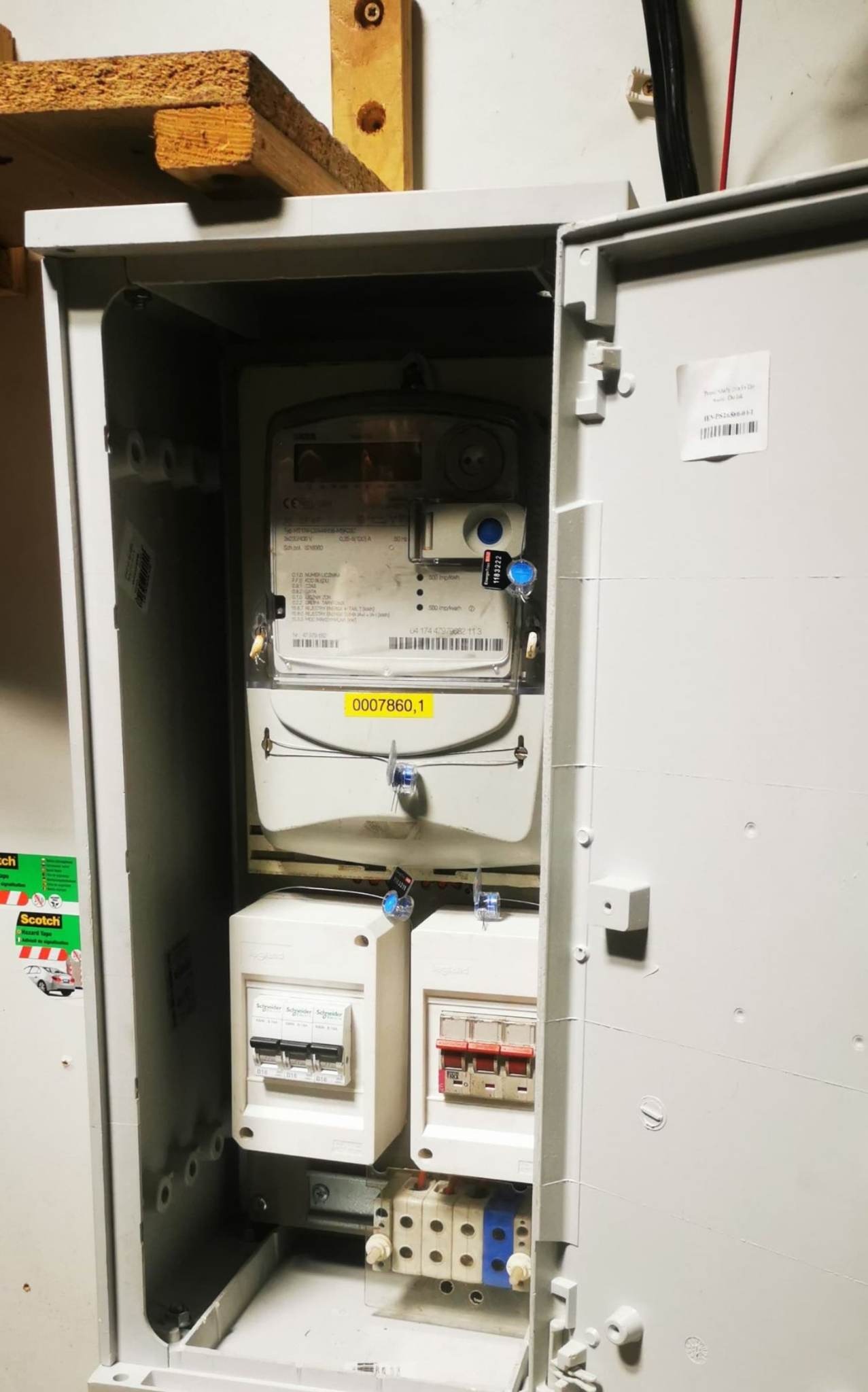 Otwarta skrzynka elektryczna z zamontowanym licznikiem energii i zabezpieczeniami, widoczne detale plomb i naklejek na liczniku.
