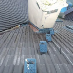 Brązowy dach z ceramicznej dachówki z zamontowanymi metalowymi stopniami kominiarskimi i kominem, widoczne ślady po myciu.